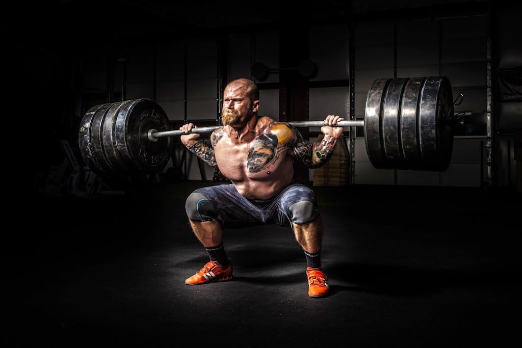 Muscular man lifting heavy weights during an intense squat session inside a gym. | This Old-School 20-Rep Squat Routine Is Still the Most Savage Leg Workout Ever