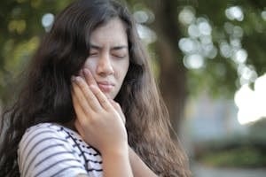 Portrait of a young woman feeling toothache, showing discomfort outdoors with a pained facial expression. | Ozempic SHOCKER: Forget "Face" – Experts Warn of a New, Hidden Danger Called "Ozempic Mouth"!