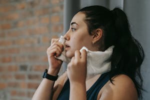 Side view of a woman wiping sweat with a towel after exercising indoors. | Body-Positive Fitness: The GENTLE At-Home Workouts for Plus-Size Bodies (Feel Great, No Pressure!)