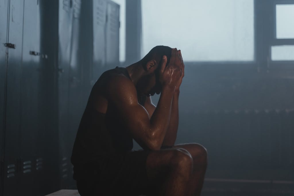 Sweaty man resting on bench in dimly lit locker room, showing exhaustion and recovery. | STOP Sabotaging Gains! 10 Post-Workout Mistakes You're Making (Beyond Just Protein) & How to Fix Them FAST
