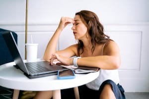 Woman experiencing work fatigue with laptop at a table, indicating stress and tiredness. | Fatigue, Weakness, and Dizziness: If You Have These Symptoms, You Are Missing This Vitamin