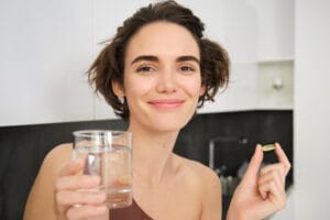 woman taking supplement with a glass of water | 5 Proven Benefits of Valerian Root (That Go Way Beyond Sleep)