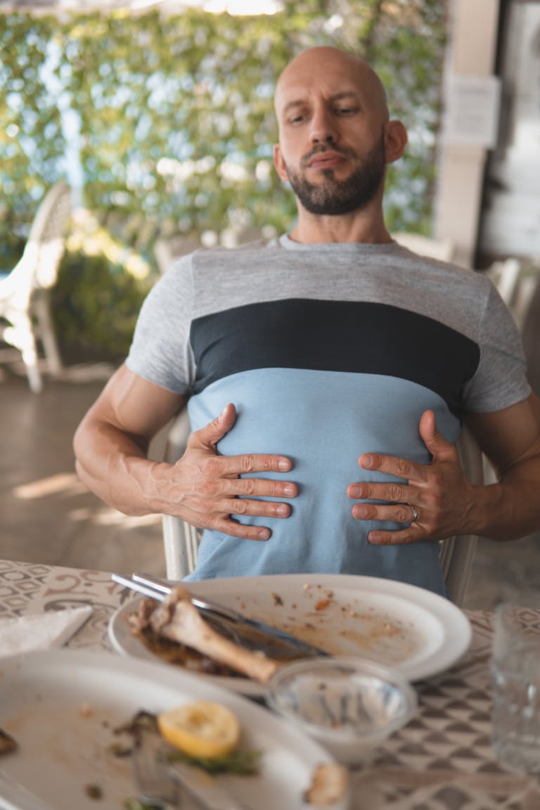 A man sits back feeling full after dining, showing a satisfied expression while touching his stomach. | Protein Overload Alert: 6 Warning Signs Your Body Is Getting TOO Much (Dietitians Say to Cut Back!)