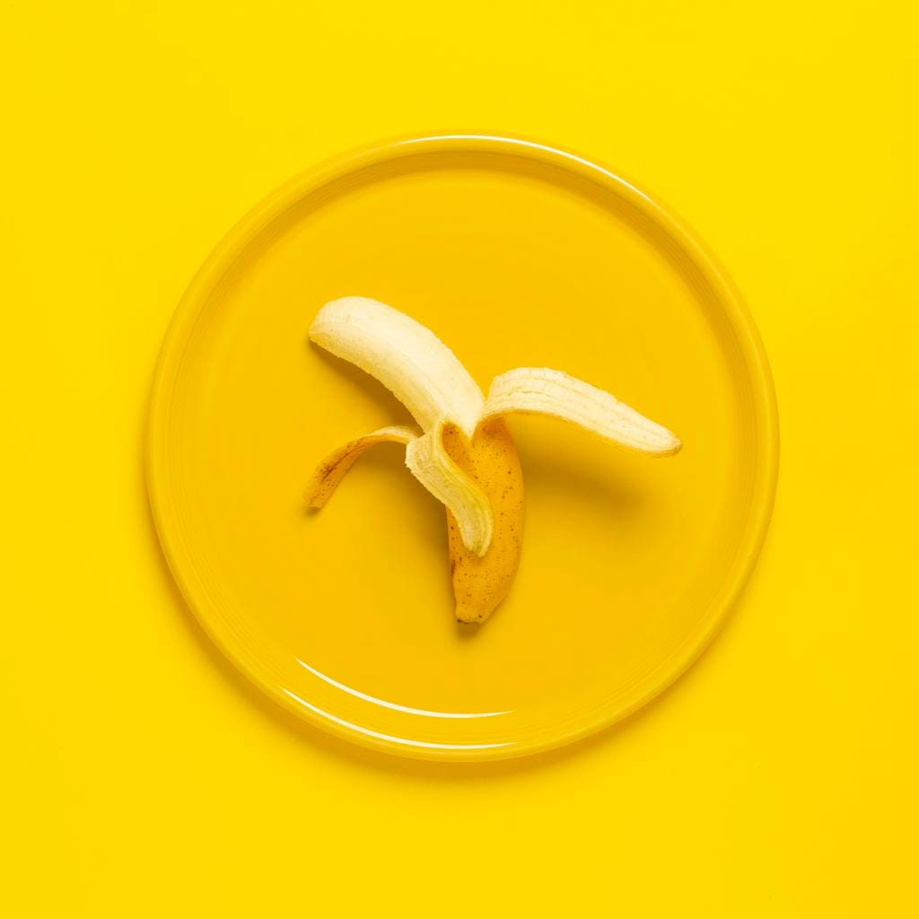 A peeled banana on a yellow plate set against a yellow background, offering vibrant color and texture contrast.