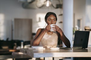 A stylish woman drinking coffee and working on a laptop indoors, creating a relaxed atmosphere. | Unlock Bone Broth's FULL Power: Drink It At THIS Specific Time for a Healthy Gut, Better Sleep & Glowing Skin!