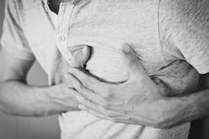 Black and white photo of a man clutching his chest, indicating discomfort or pain. | Heart Attack Foods? 7 'Healthy' Items Secretly Clogging Your Arteries (Cardiologists Warn!)