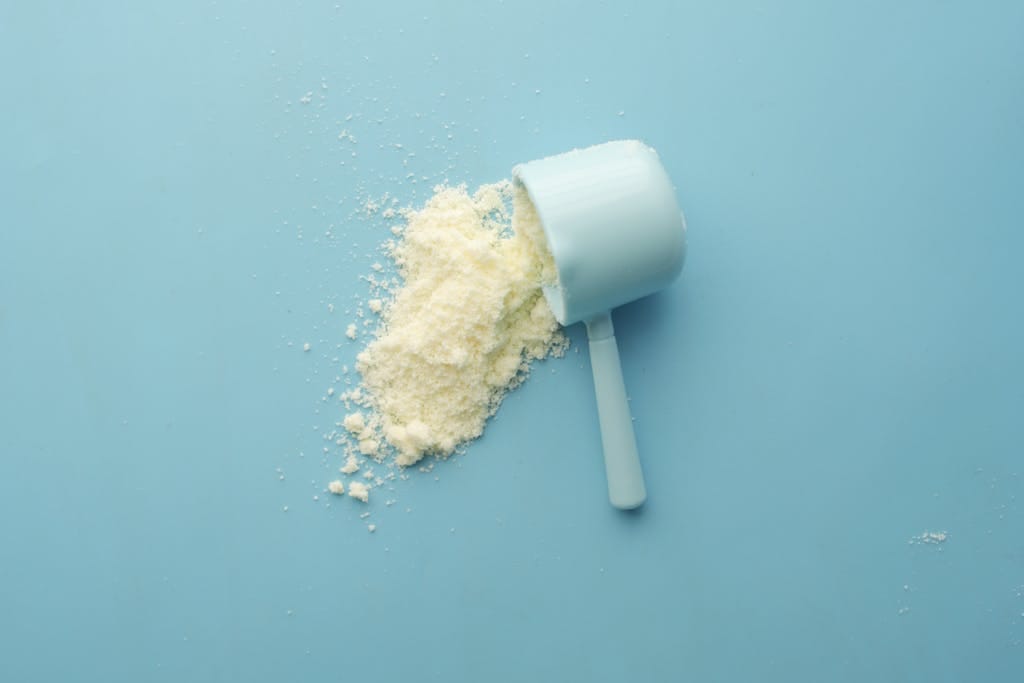 Creatine spilled from a scoop on bright blue background. Clean and minimalistic food photo.