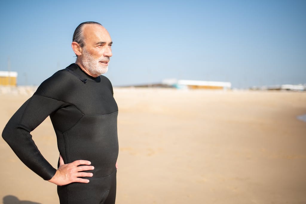 Elderly man in a wetsuit enjoying a sunny day on a Portuguese beach, ready for a swim or surf.