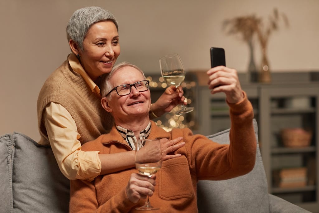 Happy senior couple capturing a memorable moment with a selfie indoors, enjoying wine together.
