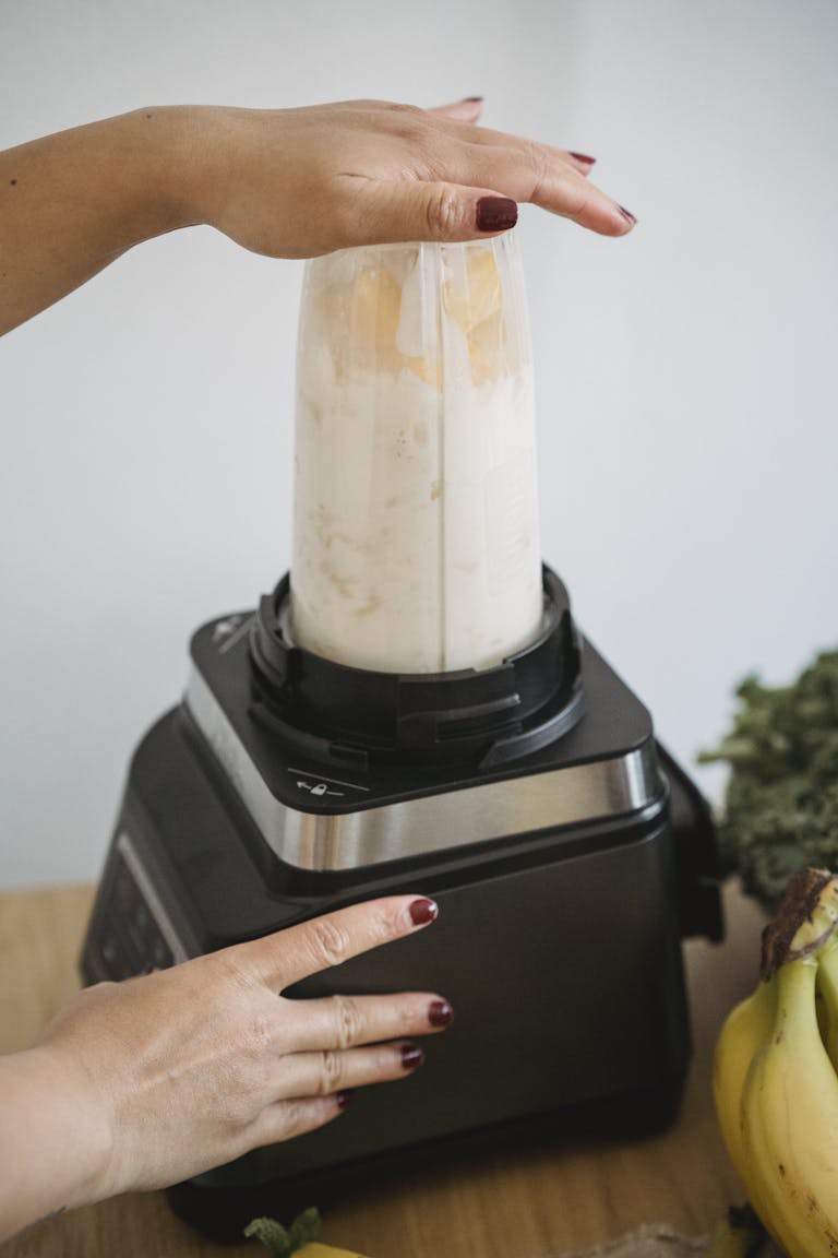 Person using a blender to prepare a fresh smoothie with bananas and kale. | Are Bananas Banned? What Experts Say About This Fruit in Your Healthy Smoothie.