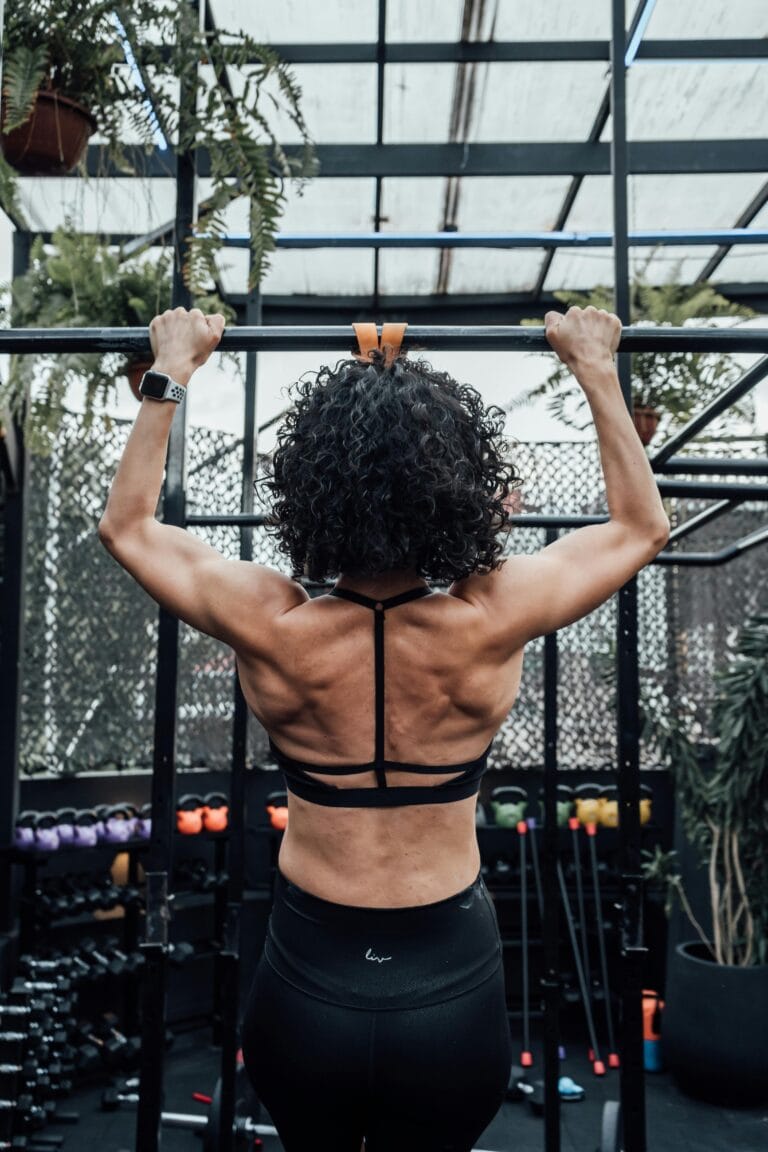 Rear view of a woman working out with pull-ups in a gym, showcasing strength and fitness. | Master Pull-ups & Forge a Monster Back: The 10-Minute Daily Method No One Tells You!