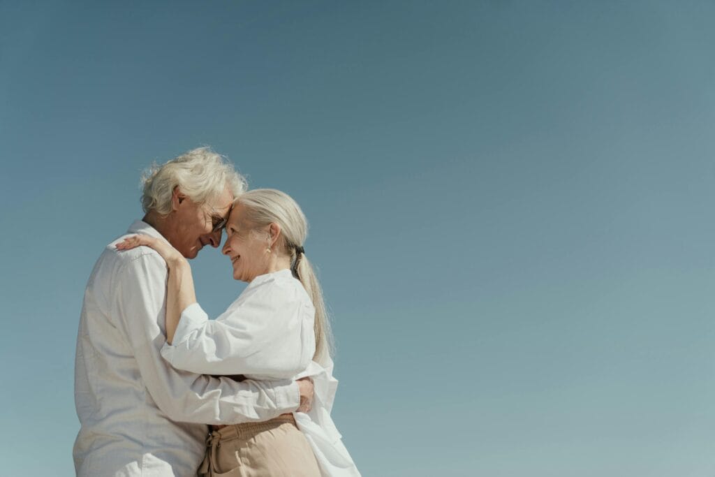 Senior couple embracing outdoors, depicting love and happiness against a clear blue sky. | If You Still Have This, You’re 2x More Likely to Live to 100, Says New Study