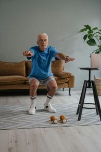 A senior man performing squats with dumbbells on a mat indoors for a healthy lifestyle. | Defy Your Age: 3 Simple Moves for Lifelong Strength & Vitality After 60