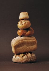 Stack of various bread loaves artfully arranged against a dark background. | The Carb Redemption: Doctors & Dietitians Say THIS "Forbidden" Carb Unlocks Longevity | sourdough bread