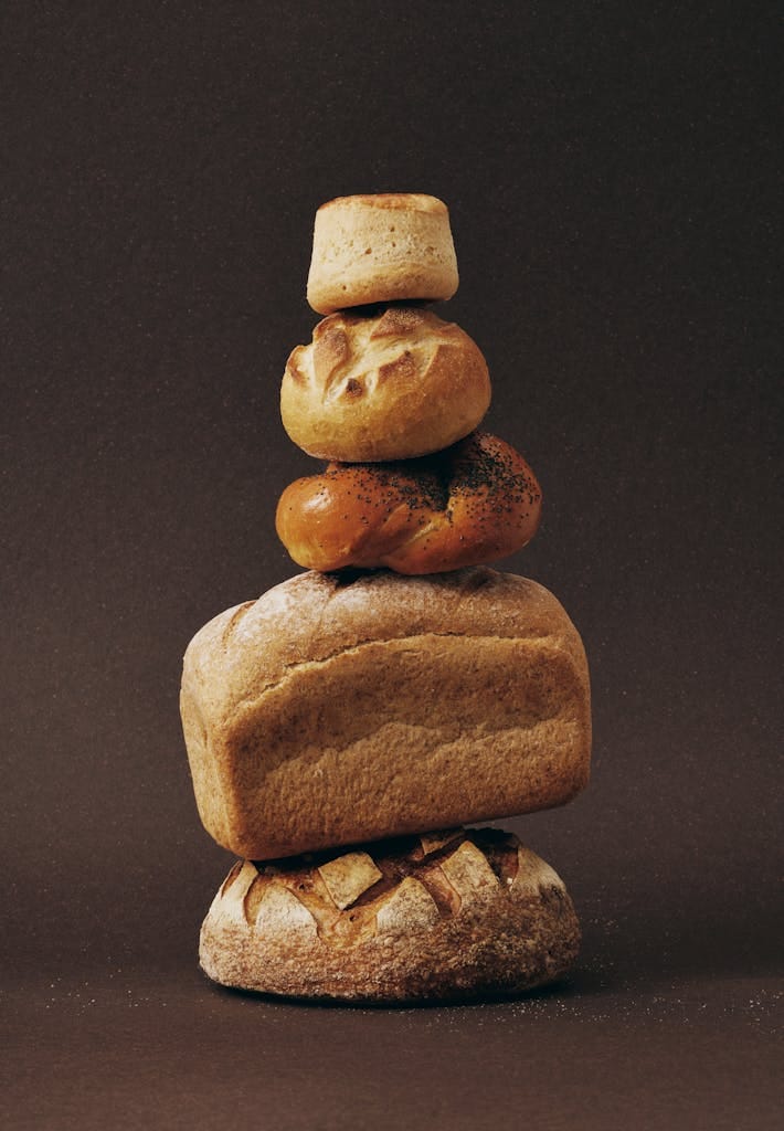 Stack of various bread loaves artfully arranged against a dark background. | The Carb Redemption: Doctors & Dietitians Say THIS "Forbidden" Carb Unlocks Longevity | sourdough bread