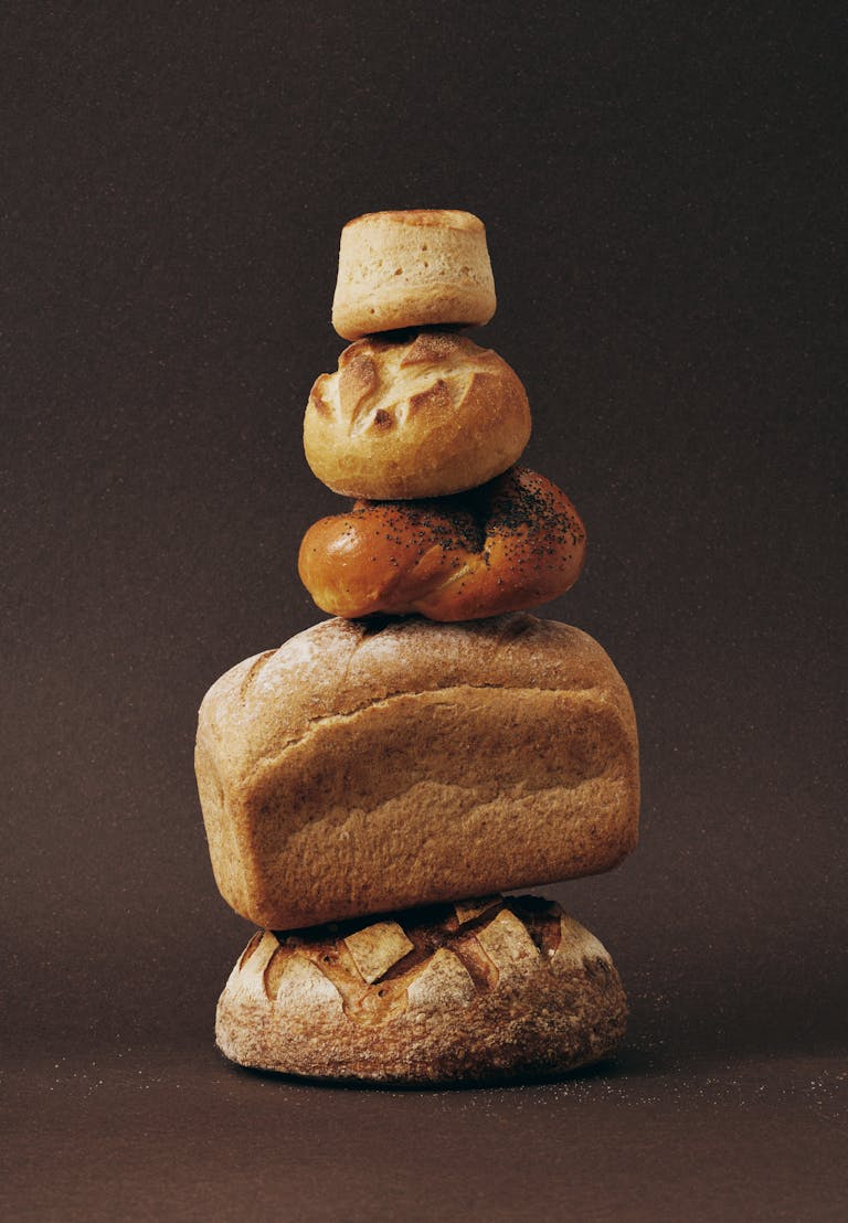Stack of various bread loaves artfully arranged against a dark background. | The Carb Redemption: Doctors & Dietitians Say THIS "Forbidden" Carb Unlocks Longevity | sourdough bread