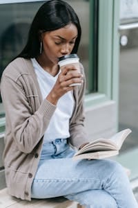 Woman sipping coffee while reading a book outdoors. Casual and relaxed scene. | Thyroid Breakthrough: Naturally END Weight Gain & Hair Loss (Your Guide to a Revived Metabolism)