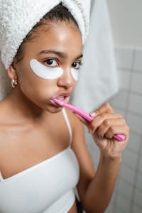 Young woman brushing teeth and applying under-eye masks for self-care. | Dentist's Warning: 3 Brushing "Mistakes" Silently Rotting Your Teeth (Stop Decay & Save Your Smile!)