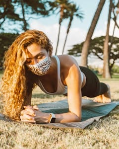 Young woman doing plank exercise on a yoga mat outdoors, wearing a protective leopard-print face mask. | Stop Guessing Your Plank Routine! PTs Share the EXACT Weekly Plan for Core Strength & Flat Abs