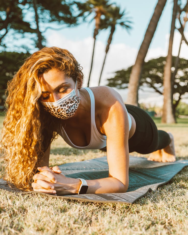 Young woman doing plank exercise on a yoga mat outdoors, wearing a protective leopard-print face mask. | Stop Guessing Your Plank Routine! PTs Share the EXACT Weekly Plan for Core Strength & Flat Abs