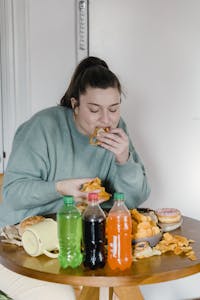Young woman enjoys assorted fast food and snacks indoors with a variety of sodas. | Diabetes Alert: Why Sweet Drinks Are WORSE Than Solid Sweets for Your Blood Sugar (And How to Escape!)
