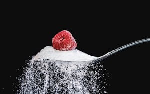 A vibrant raspberry resting on a sugar-coated spoon against a black backdrop. | Sweet Victory: 7 Natural Sweeteners That Taste Incredible & Keep Your Blood Sugar Flat