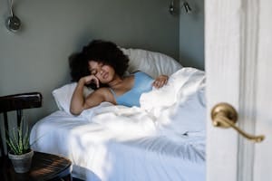 A woman peacefully sleeping in a cozy bedroom with natural light and white linens. | Your Favorite Sleeping Position Is Secretly RUINING Your Health