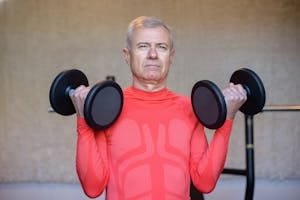 Elderly man in red lifting dumbbells, promoting fitness and healthy aging indoors. | Defy Your Age: 4 Simple Strength Workouts to Build Muscle & Stay Strong After 50