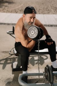 Elderly man lifting weights shirtless in park, showcasing fitness lifestyle. | Defy Age: 4 Strength Workouts to Rebuild Muscle & Boost Vitality After 50