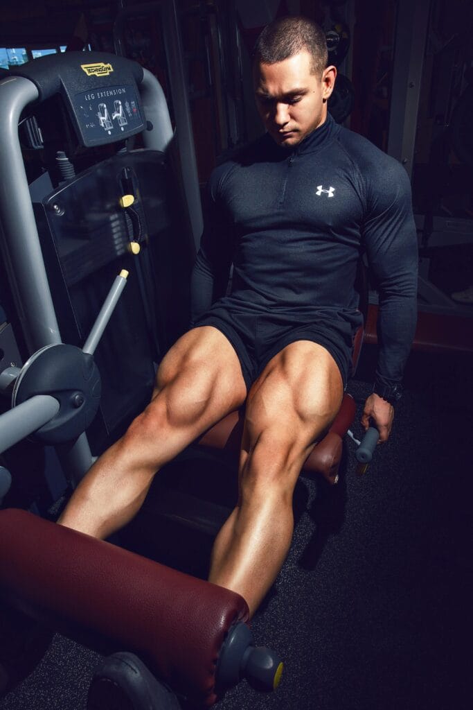 A muscular man working out on a leg extension machine in a gym setting, showcasing strength and fitness. | The Scientist-Backed Leg Day Hack: Curls BEFORE Squats for Explosive Hamstring Growth & Less Fatigue