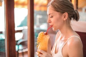 A young woman sips a refreshing citrus drink with a straw indoors, enjoying a warm and sunny day. | 20 Lazy Ways to Shed Pounds (You Won't Even Feel Like You're Dieting!)