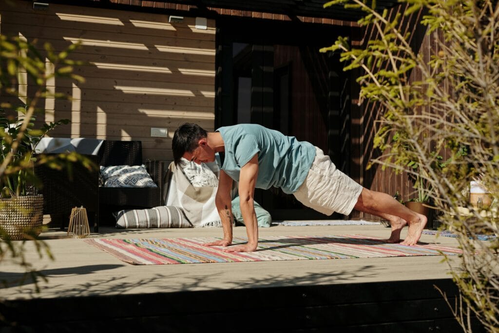 Adult man doing a plank exercise on a colorful yoga mat outdoors, promoting fitness and healthy living.