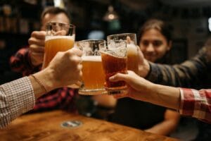 Celebratory toast with beer mugs among friends indoors, capturing fun and friendship. | Wrecking Your Gut? Avoid These 5 Common Habits That Cause Bloating, Brain Fog & More
