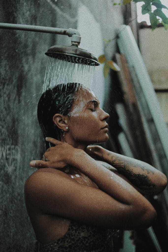 Tattooed woman relishing a refreshing outdoor shower in a serene setting.