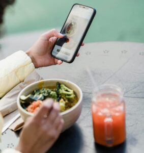 Crop unrecognizable female blogger touching screen on cellphone above street cafe table with healthy food and smoothie | Ditch Pain & Bloat: The Dietitian's 30-Day Zero-Sugar Anti-Inflammatory Meal Plan