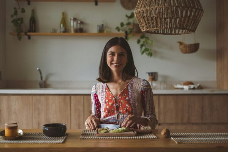 A woman smiles while preparing food in a warm and inviting kitchen setting. | The Gut Health Game-Changer? This Obscure Fiber Feeds Your Good Bacteria Like Nothing Else