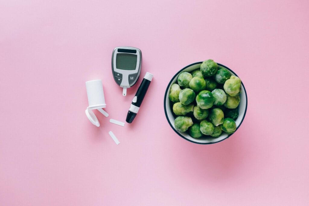 Top view of a glucometer and fresh Brussels sprouts on a pink background promoting health. | Eat These 5 Foods Daily to Naturally Lower Blood Sugar & Boost Insulin Sensitivity