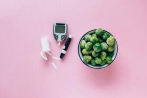 Top view of a glucometer and fresh Brussels sprouts on a pink background promoting health. | Eat These 5 Foods Daily to Naturally Lower Blood Sugar & Boost Insulin Sensitivity