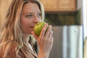 Close-up of a woman enjoying the fresh scent of a green apple indoors. | Gut-Friendly Carbs: The 6 Foods Dietitians Recommend To Help You Poop