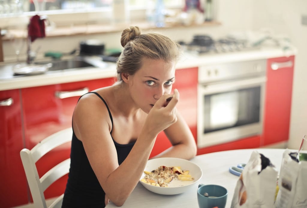 Woman eating a healthy breakfast with cereal and milk at a kitchen table.