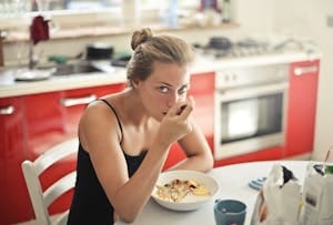Woman eating a healthy breakfast with cereal and milk at a kitchen table. | Is Oatmeal Good for Diabetics? The Best Way To Eat It Without Spiking Your Blood Sugar