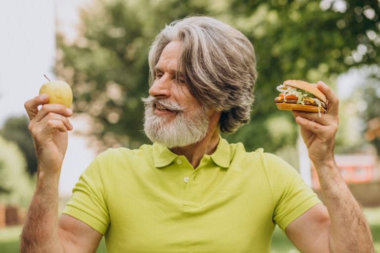 elderly man choosing between an apple and a burger | 10 Anti-Aging Superfoods That Could Add Years to Your Life (Science Says So)