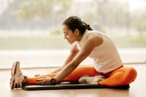 A woman performing a hamstring stretch indoors, promoting fitness and flexibility. | Sore and Stiff? These 11 Recovery Foods Work Better Than Stretching