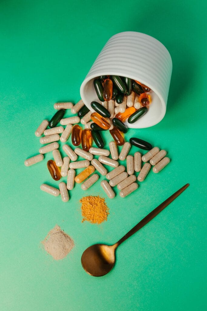 Colorful capsules and powders on a green background with a spoon, ideal for health or supplement themes.