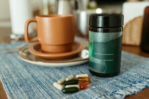 A variety of capsules near a ceramic mug and container on a table. | Your Morning Coffee Could Be Canceling Out Your Vitamins—Here’s What You Need to Know