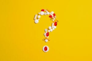 Assorted pills and capsules arranged in a question mark on a bright yellow background symbolizing medication inquiries. | Warning: Your Daily Vitamin Habit Could Be Fueling Cancer, New Research Reveals