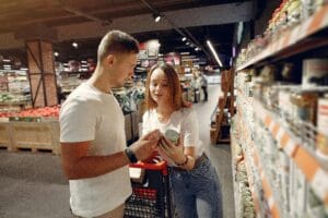 A young couple looking at canned goods in a supermarket aisle, shopping together. | These 10 Canned Foods at Walmart Are Too Good (and Cheap) to Ignore