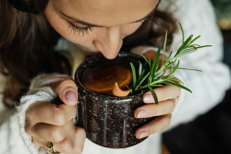 Woman savoring hot herbal tea with rosemary and orange, close-up view. | Gut Expert's Secret: 10 Evening Habits to Guarantee a Morning Poop