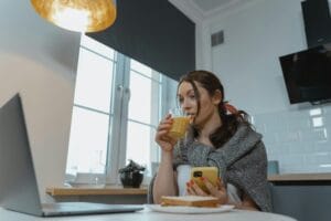 Woman sitting indoors, sipping juice and browsing on her smartphone.