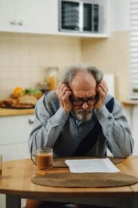 Senior man looking stressed while reading documents in a kitchen setting, suggesting financial or personal concerns. | This Is the Exact Age Your Brain Begins to Decline—And What You Can Do About It